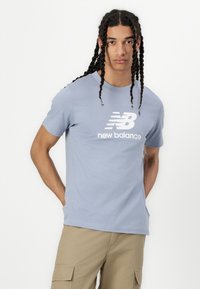 Világoskék pamut póló, fehér "New Balance" logóval a mellrészen. Rövid ujjú és kerek nyakú.