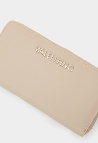 Billetera de cuero beige con un acabado texturizado, que presenta un cierre con cremallera y el logo "VALENTINO" grabado en letras metálicas.