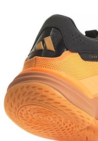 Nahaufnahme der Ferse eines orange-schwarzen Sportschuhs mit strukturiertem Sohlenprofil und Adidas-Logo auf dem schwarzen Fersenteil.