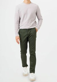 Ljusgrå stickad tröja med långa ärmar, som är kombinerad med slim-fit mörkgröna byxor och vita sneakers med beige detaljer.