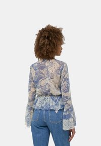 Blusa trasparente con motivo floreale in blu chiaro e crema, con maniche lunghe e svasate e orlo arricciato. Abbinata a jeans in denim a vita alta.