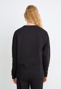 Sudadera negra con cuello redondo, mangas largas y puños acanalados. Textura suave y mínimo detalle, vista desde la parte de atrás.