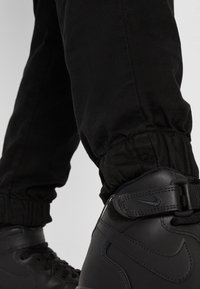 Baskets montantes noires en cuir texturé, avec un design à lacets et une bande Velcro, associées à un pantalon noir fuselé avec des poignets élastiques.