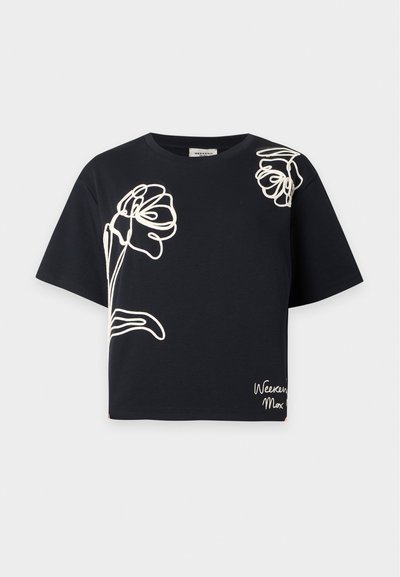Crop top noir à manches courtes avec des dessins abstraits floraux blancs au trait sur le devant et l'épaule droite supérieure, et petit texte blanc en cursive près de l'ourlet.