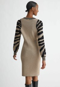 Abito a maglia caratterizzato da un corpo con lucentezza dorata, maniche a strisce nere e dorate, scollatura rotonda e forma aderente. Accessori non visibili.