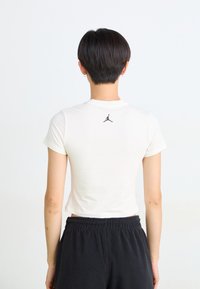White cropped t-shirt with short sleeves, featuring a black Jordan logo on the back, paired with dark sweatpants. Smooth texture.