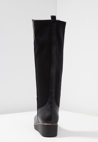 Stivale nero alto fino al ginocchio realizzato in pelle liscia e tessuto elasticizzato. Caratterizzato da un tacco a zeppa basso, cuciture verticali e un asola per una facile calzata.