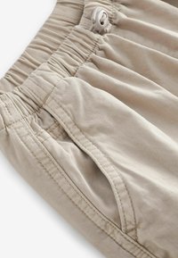 Beige shorts med elastisk talje, snøre lukning og sidelommer. Stof har en glat tekstur og synlige syningsdetaljer.