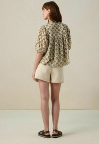 Korte mouw, gebloemde blouse met een geplooide achterkant, versierd met palmbomenmotieven in groen en bruin op een beige achtergrond, gecombineerd met crèmekleurige shorts.