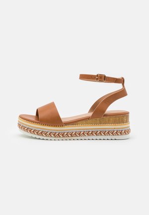 Bruine leren sandaal met een enkelbandje, een chunky geweven platform met zigzagdetails en een witte rubberen zool.