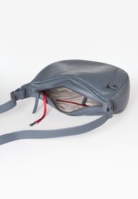 Grijze leren tas met een gebogen vorm, voorzien van een open bovenkant en een binnenvak met rits met een rode accent en een gladde stoffen voering.
