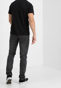 Svart t-shirt med kort ärm, åtsittande modell. Kombinerad med mörkgrå slim-fit jeans. Svarta sneakers med vita detaljer, synliga från baksidan.