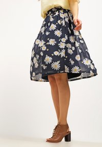 Gonna floreale blu navy con margherite bianche, tessuto trasparente, vita arricciata, lunghezza al ginocchio, abbinata a scarpe con tacco in pelle marrone con lacci.