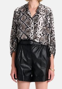 Blusa a maniche lunghe, dalle linee morbide, con stampa a serpente nei toni di nero, bianco e beige; abbinata a pantaloni shorts in pelle nera a vita alta.