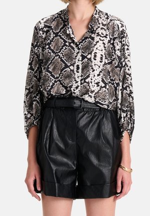 Blusa a maniche lunghe, dalle linee morbide, con stampa a serpente nei toni di nero, bianco e beige; abbinata a pantaloni shorts in pelle nera a vita alta.