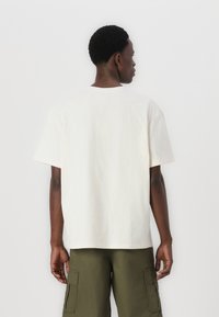 Off-white bomulds t-shirt med afslappet pasform, rund hals og korte ærmer, parret med olivengrønne cargo-bukser med sidelommer.