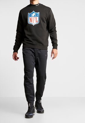 Sudadera negra con el logo de la NFL en colores, combinada con pantalones deportivos negros y zapatillas negras con acentos texturizados.