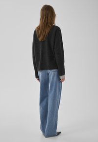 Dunkelgrauer Pullover aus weichem Material mit lockerem Schnitt. Kombiniert mit hellblauen Jeans mit weitem Bein und verwaschenem Look.