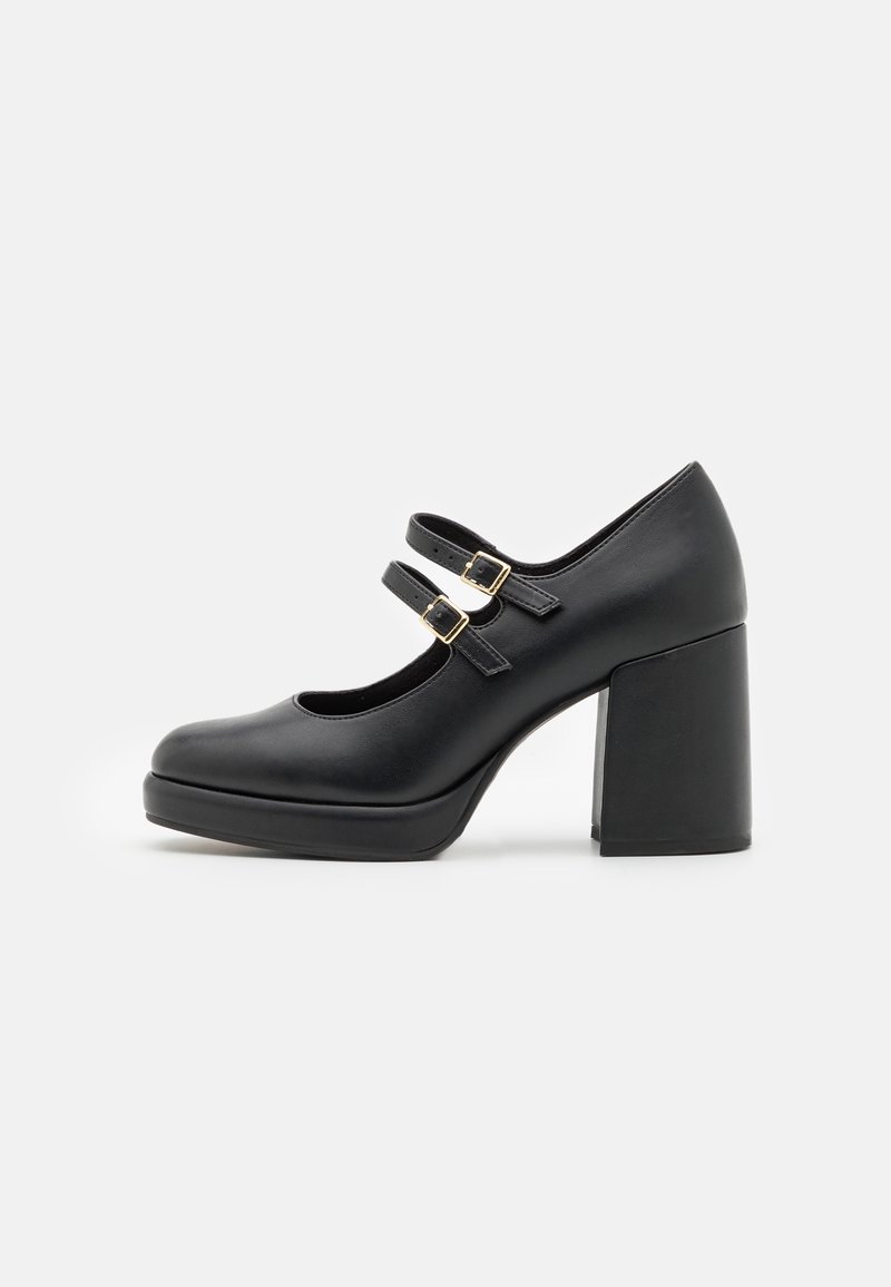 Chaussure Mary Jane en cuir noir avec deux brides à boucle et un talon haut épais sur fond blanc.