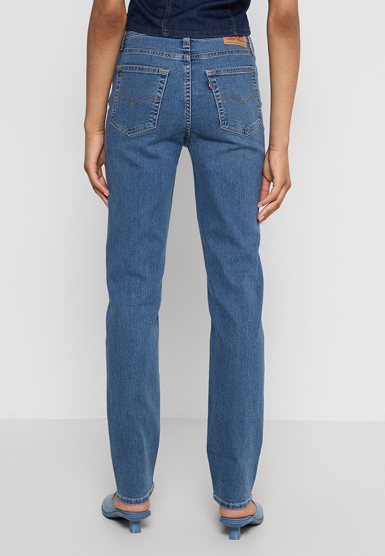 Jeans in denim blu con una vestibilità dritta, due tasche posteriori, cuciture visibili e un logo in pelle applicato sulla vita. Nessun altro dettaglio visibile.