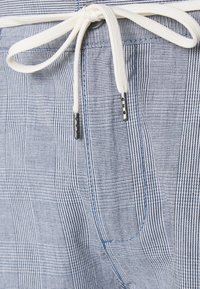 Blå och vit randig tyg med en framficka och vit snörning knuten i en rosett med metalländar.