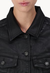 Giacca in denim nero con colletto classico, due tasche sul petto e dettagli in metallo con finitura testurizzata.
