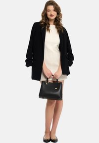 Blazer nero su un vestito crema, abbinato a una borsa nera e a scarpe flats nere con accenti dorati. Il tessuto strutturato e la vestibilità su misura sono notevoli.