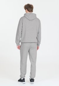 Harmaa puuvillane kapuutsiga sweatshirt, millel on kängurupocket, millele on sobitatud sobivad dressipüksid. Omab soonikvarrukate ja reguleeritava kapuutsi funktsioone. Jalatsiteks: mustad jooksujalanõud.