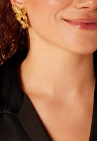 Gouden vlinderoorbellen hebben ingrijpende ontwerpen met gestructureerde vleugels. De grotere vlinder zit bovenop een kleinere, wat de gedetailleerde accenten benadrukt.