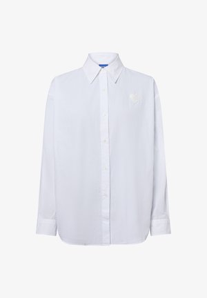 Weißes Langarmhemd mit Knopfleiste und spitzem Kragen sowie einem kleinen herzförmigen gestickten Patch auf der linken Brust.