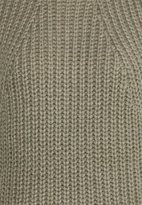 Primo piano di un tessuto di maglia beige con una texture a coste e un motivo di cucitura verticale.