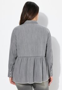 Blusa peplum grigia realizzata in tessuto leggero. Caratterizzata da un colletto, maniche lunghe con polsini bottonati e orlo sfilacciato per un tocco di texture.