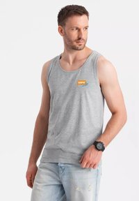 Šedý bavlněný top na ramínka s tištěným logem v oranžové a tyrkysové barvě. Nosit s odřenými světle modrými džíny a černými hodinkami.