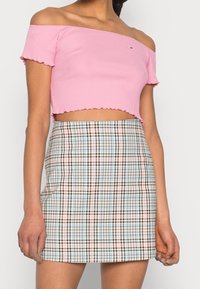 Růžový průsvitný crop top bez ramínek s volánkovým lemem, kombinovaný s károvanou sukní v modrých, hnědých a krémových barvách.