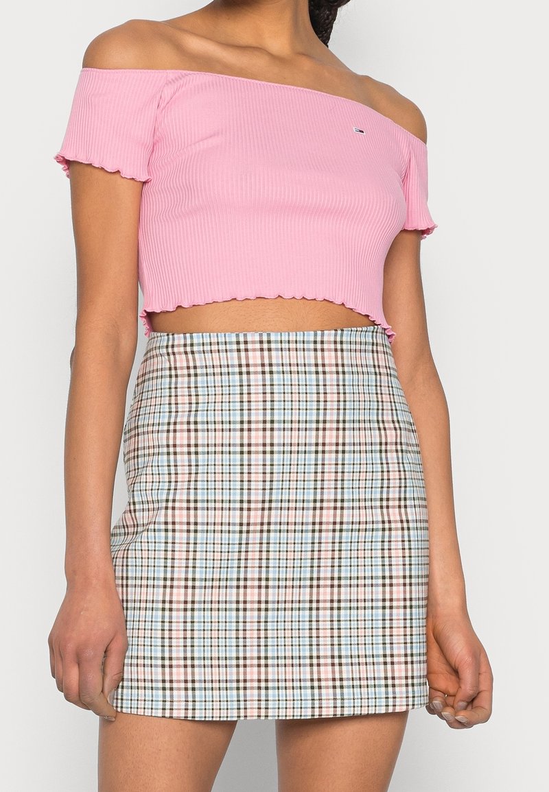 Růžový průsvitný crop top bez ramínek s volánkovým lemem, kombinovaný s károvanou sukní v modrých, hnědých a krémových barvách.