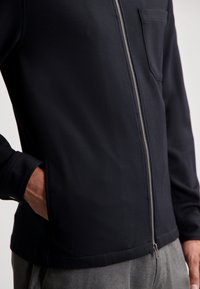 Chaqueta azul marino con cremallera, fabricada en un tejido texturizado, con un bolsillo en el pecho y un corte ajustado. Presenta un diseño limpio y moderno, combinado con pantalones grises en contraste.