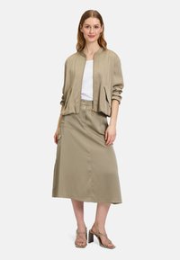 Giubbotto bomber khaki con zip frontale, abbinato a una gonna coordinata lunga fino al ginocchio. Tessuto liscio, polsini a coste e design minimalista.
