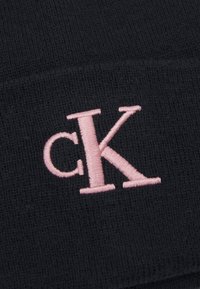 Fekete kötött beanie, amelyen egy feltűnő rózsaszín hímzett "cK" logó található. A textúra bordázott, így szoros illeszkedést biztosít.