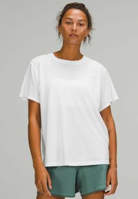 Witte katoenen t-shirt met korte mouwen, ronde hals, relaxte pasvorm, gedragen met groene shorts. Glad textuur, geen zichtbare patronen of accenten.