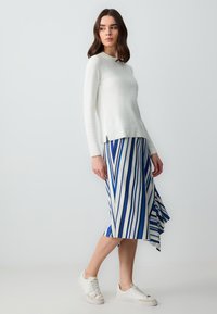 Haut à manches longues blanc associé à une jupe rayée bleu et blanc, présentant un ourlet fluide et des baskets blanches. Design simple et moderne.