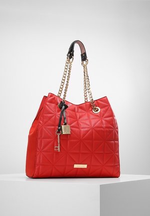 Sac à main en cuir rouge matelassé avec des brides en chaîne dorée, une poignée en cuir noire et des breloques décoratives en forme de clé et de serrure dorées.