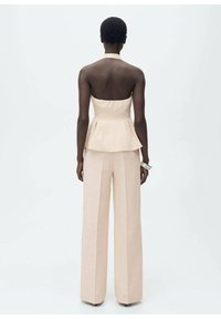 Peplum top z měkké béžové látky bez ramínek, spárovaný s kalhotami s širokými nohavicemi ve shodné barvě; hladká textura a přiléhavý střih.