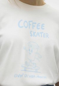 Witte katoenen t-shirt met een blauwe grafische print van een skateboardende koffiekop, met tekst "COFFEE SKATER" en "LIVIN' LA VIDA MOCHA" eronder.
