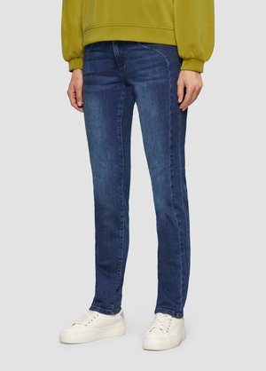 Jean en denim slim fit bleu foncé, avec un design classique à cinq poches et des coutures contrastantes. Associé à des baskets blanches.