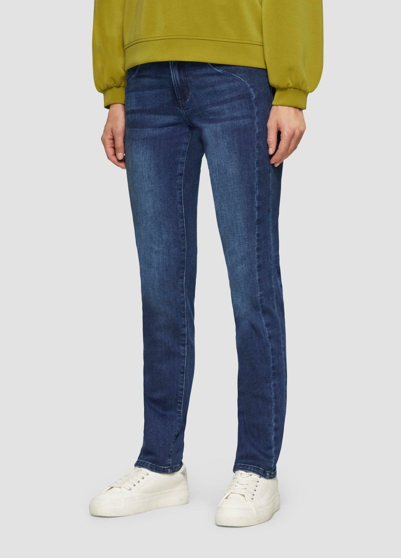 Slim-Fit-Denim-Jeans in Dunkelblau, mit einem klassischen Fünf-Taschen-Design und kontrastierenden Stichdetails. Kombiniert mit weißen Sneakern.