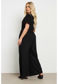 Mono negro de pierna ancha con mangas cortas y cinturilla elástica. Tejido suave con un ajuste holgado, que incluye bolsillos laterales.