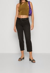 Top corto de color verde oliva con detalle de ojal, combinado con jeans negros de tobillo y sandalias de tacón bloque gris. Accesorio de bolso con flecos morado.