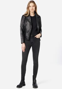 Schwarze Lederbikerjacke mit gerippten Schulterakzenten, kombiniert mit schwarzen Skinny-Jeans und schwarzen Stiefeletten. Darunter ein einfaches schwarzes Oberteil.