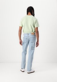 Light green short-sleeve t-shirt paired with light blue denim jeans featuring multiple pockets and a tan leather tag on the back.