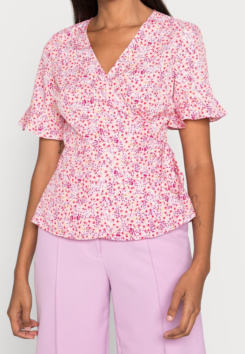 Haut portefeuille à imprimé floral rose et blanc, manches courtes à volants, col en V, taille cintrée, tissu léger, associé à un pantalon lavande.